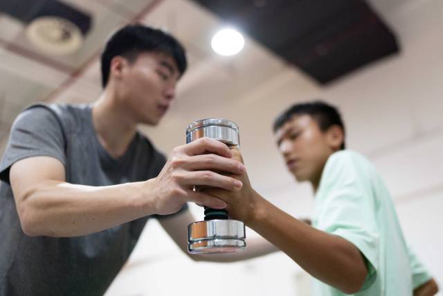 在结束早午两操后，助教林琪深单独留下钟英杰，帮助他用哑铃加练手臂伸展力量。