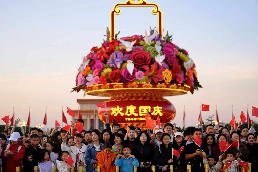 2025年10月1日，在北京天安门广场，人们观看升国旗仪式后挥舞国旗。